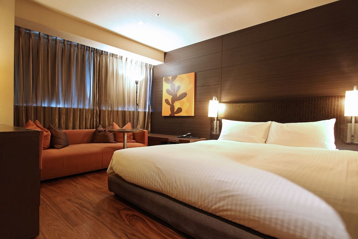 Habitación de hotel con una cama grande, un sofá, un escritorio y una obra de arte colgada en la pared.