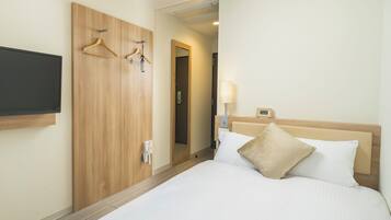 A hotel room with a bed, a TV mounted on the wall, wooden wardrobe, and a mirror.