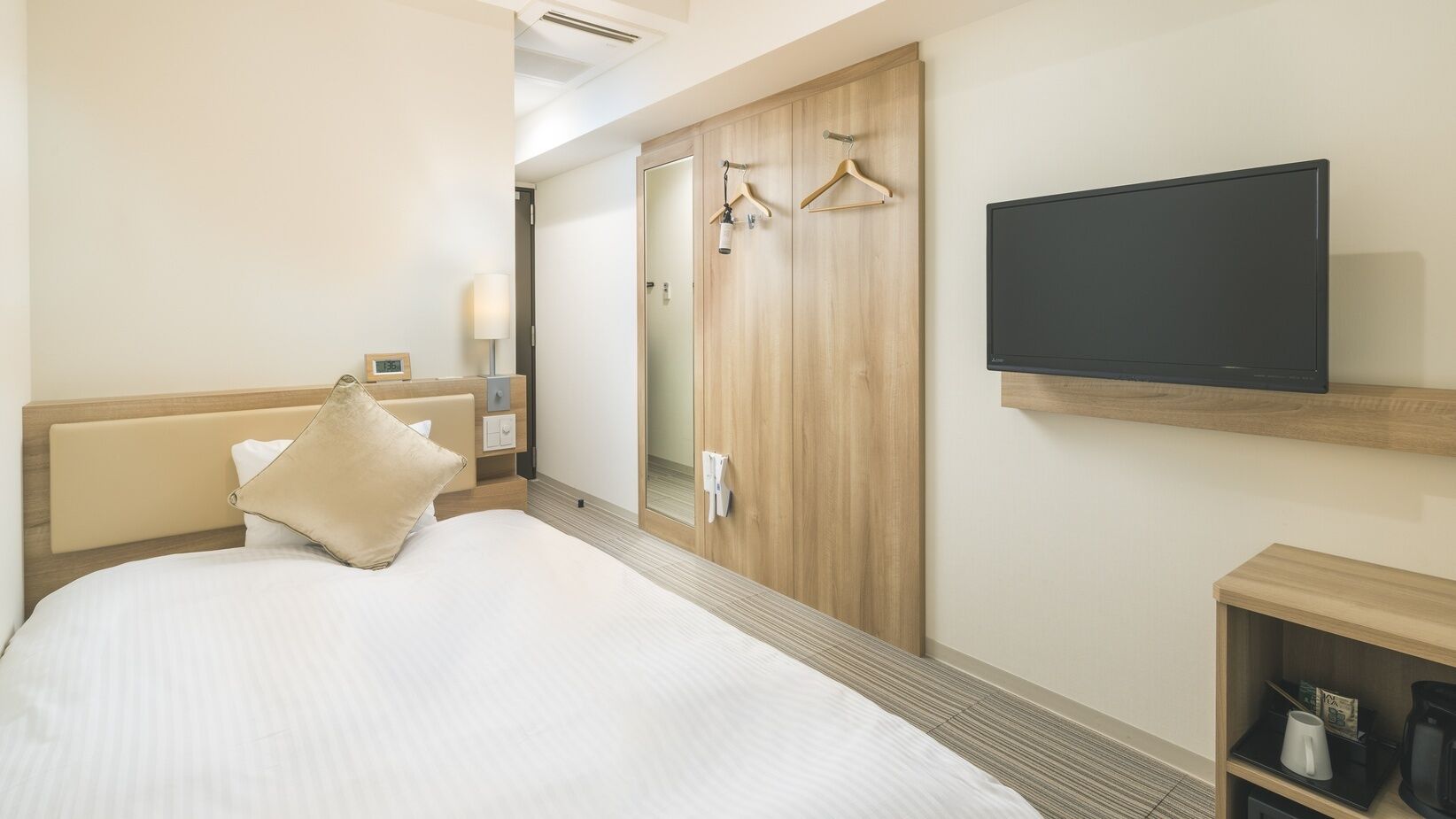 A hotel room with a bed, a TV, a wardrobe, and a small shelf with items.