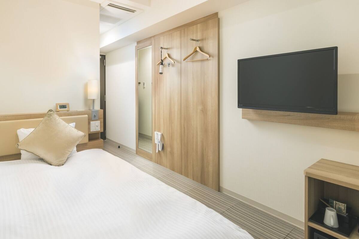 A hotel room with a bed, a TV, a wardrobe, and a small shelf with items.
