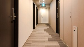 Un pasillo de hotel con alfombra estampada, puertas a ambos lados y un letrero de salida iluminado en el techo.