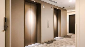 A hallway with three elevator doors, a control panel, and a patterned carpet.