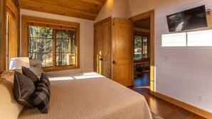 A bedroom with a large bed, a wooden ceiling, and a TV mounted on the wall.