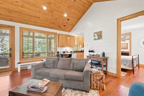 Ein modernes Wohnzimmer mit grauem Sofa, Holzböden und großen Fenstern.