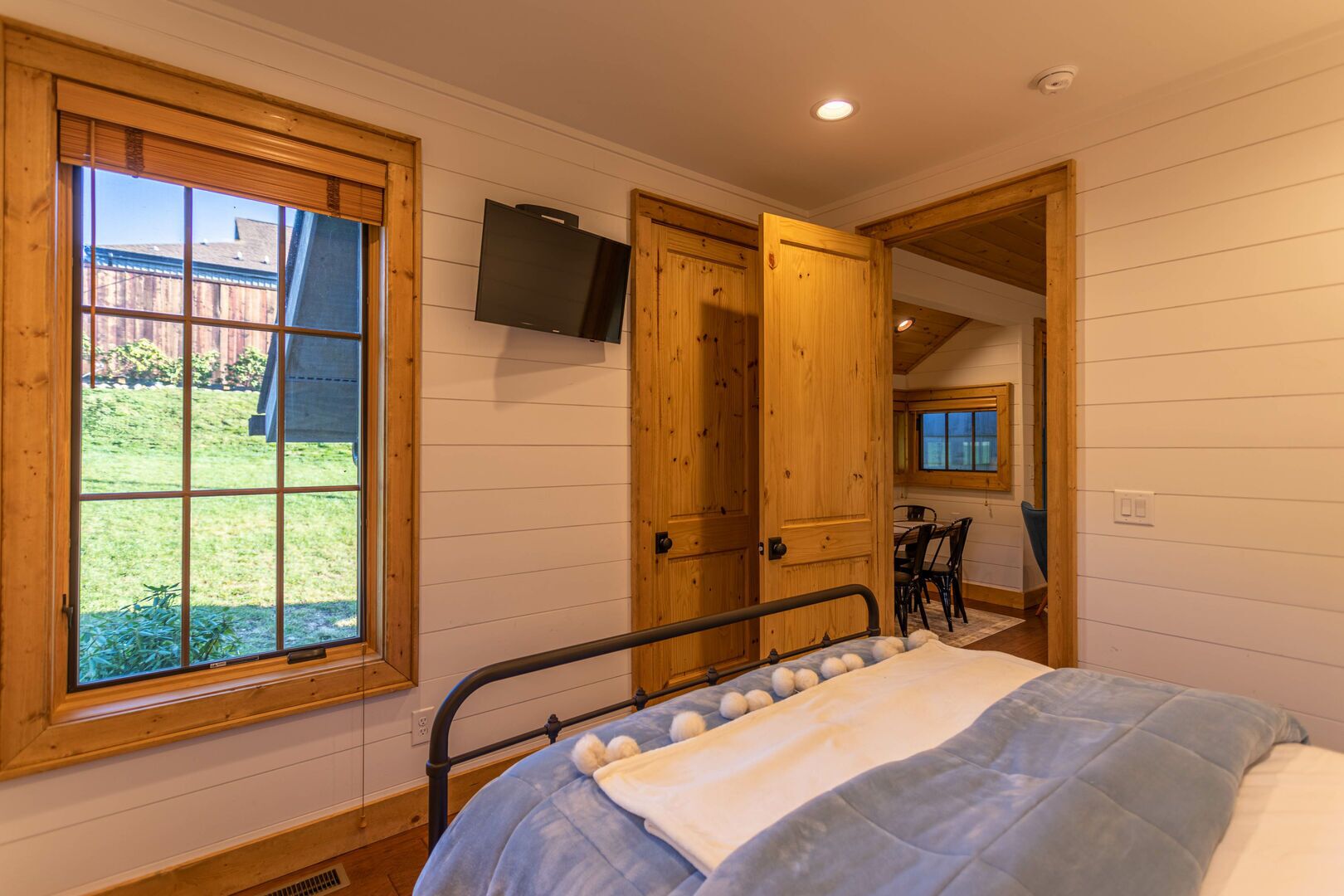 A bedroom with a bed, a TV mounted on the wall, and a window with a view of the outside.