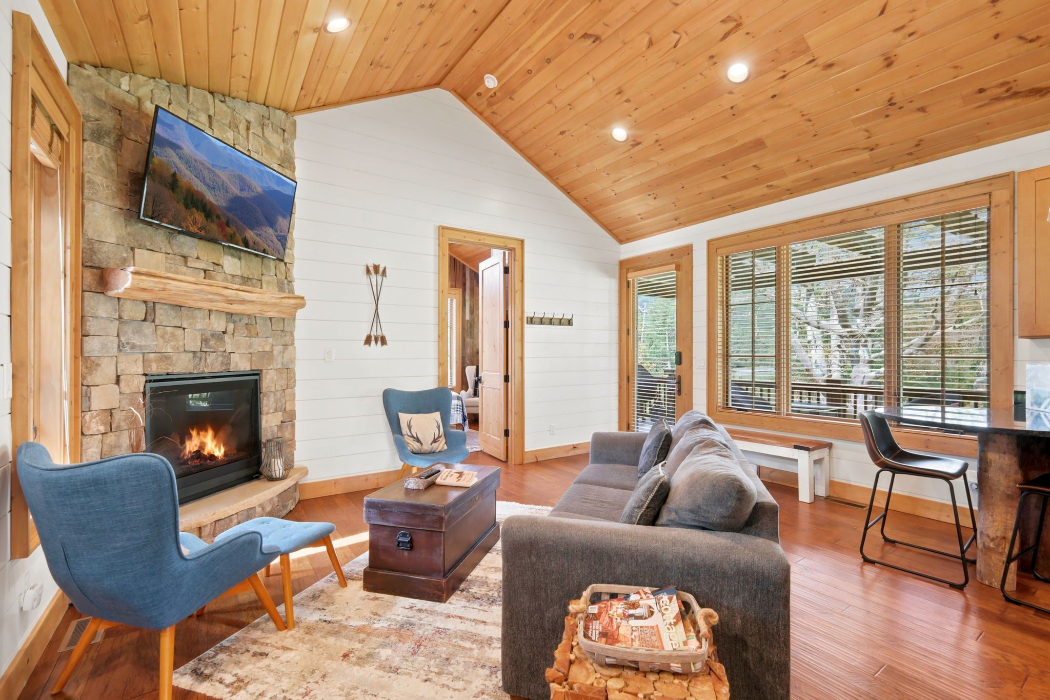 A cozy living room with a stone fireplace, comfortable seating, and large windows.
