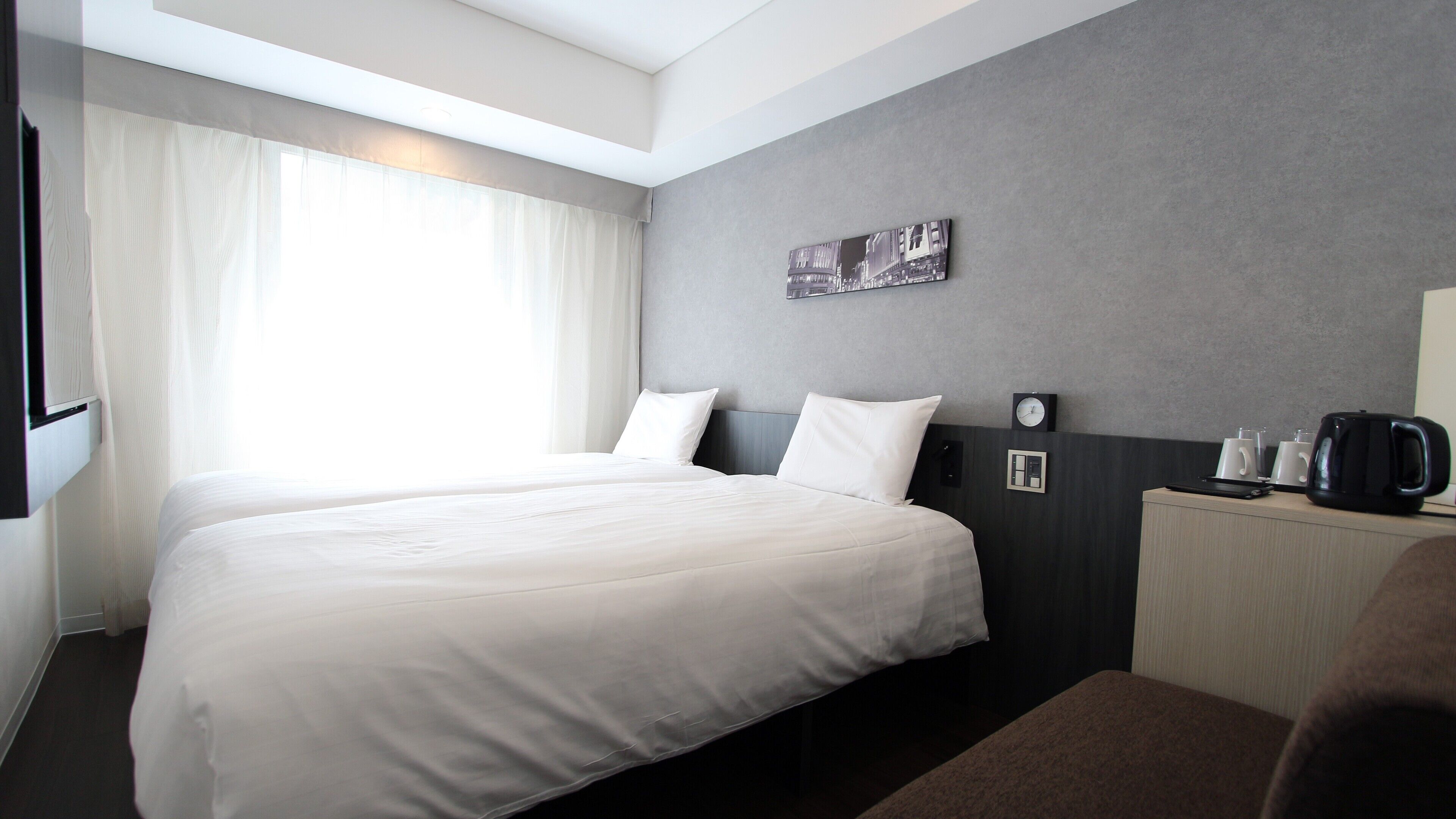 Une chambre d’hôtel avec un grand lit, une table de chevet avec une machine à café, une horloge et un tableau au mur.