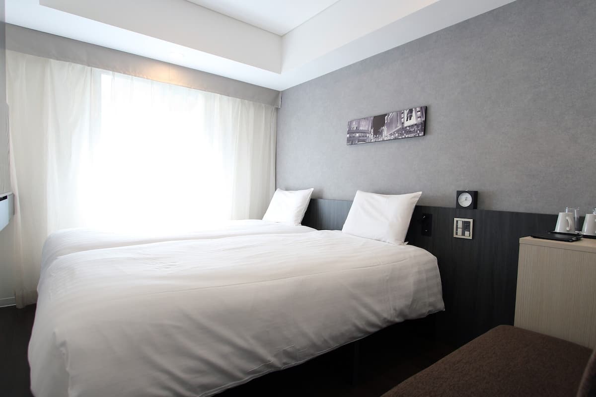 A hotel room with a large bed, a bedside table with a coffee maker, a clock, and a painting on the wall.
