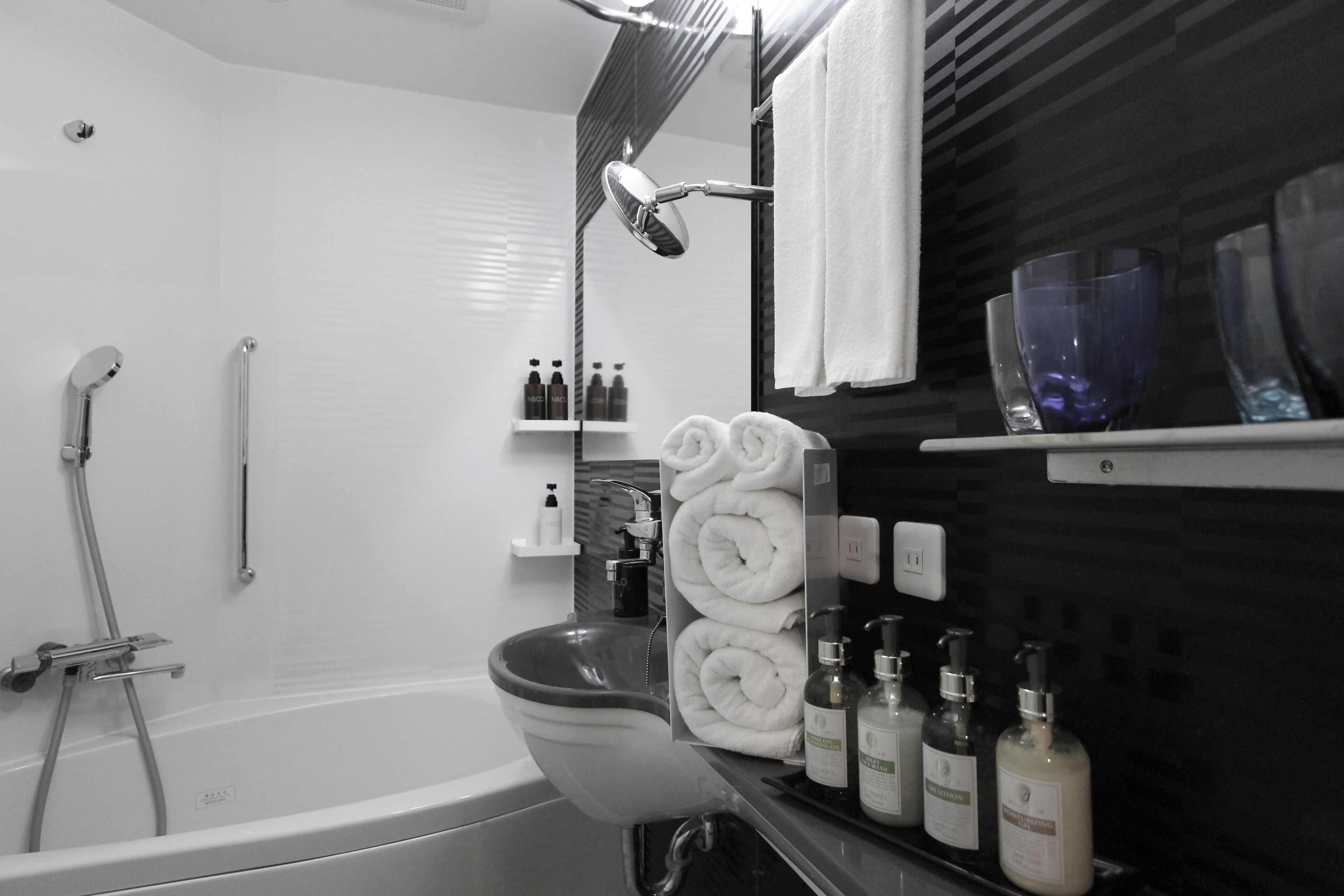 A modern bathroom with a bathtub, a toilet, and a shower area. There are towels, toiletries, and a mirror on the counter.