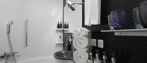 A modern bathroom with a bathtub, a toilet, and a shower area. There are towels, toiletries, and a mirror on the counter.