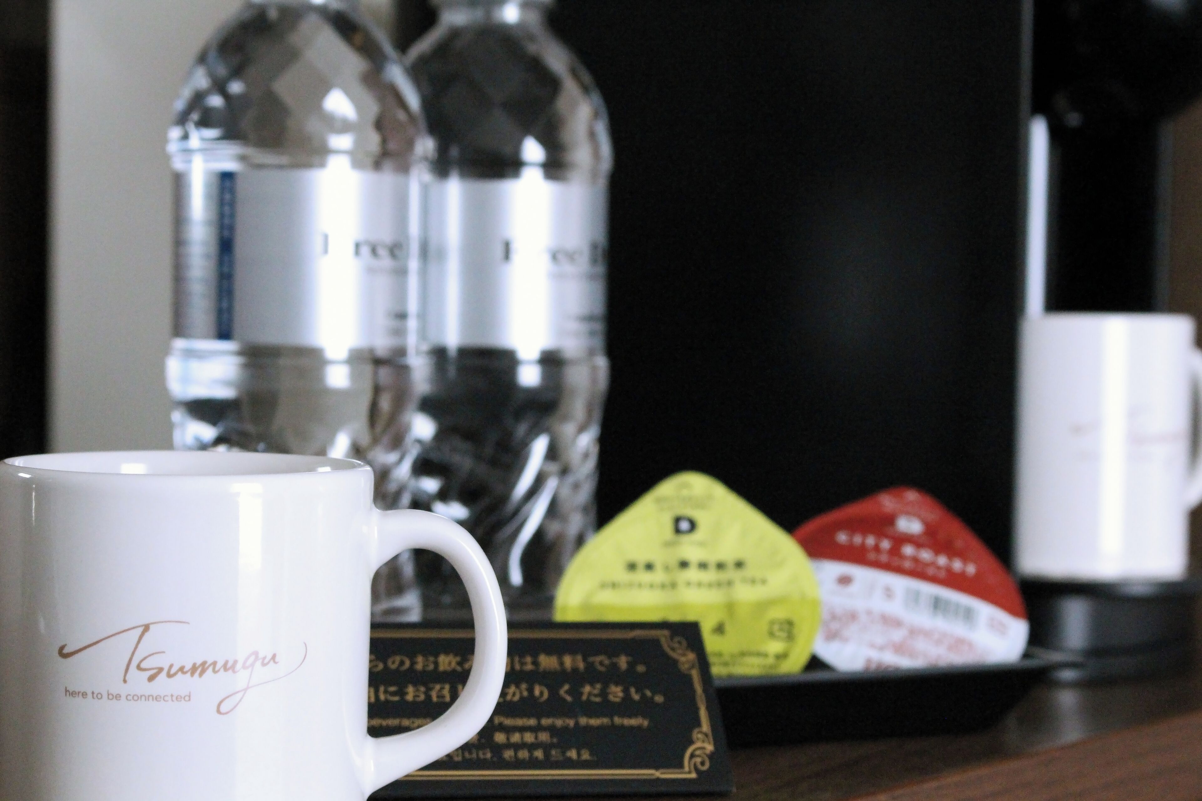 A white mug with the text "Tsumugu here to be connected" and a tray with a yellow packet and a red packet.