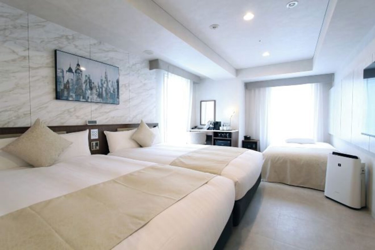 Habitación de hotel con dos camas, un escritorio y vistas a la ciudad.