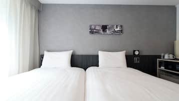 A double bed with white linens, a gray headboard, a clock, and a small table with a coffee maker.