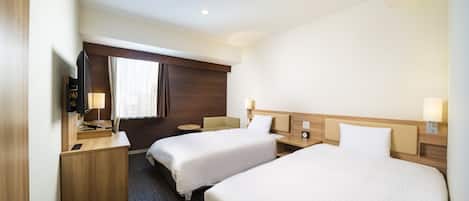 A hotel room with two single beds, a desk, a chair, a TV, and a window with curtains.