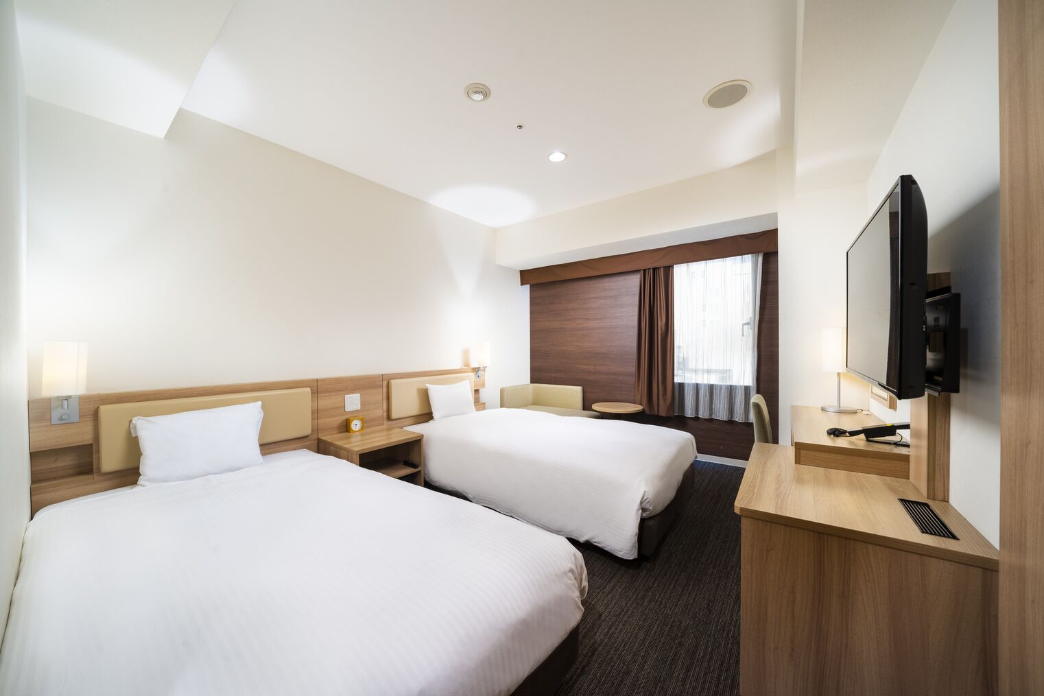 Een hotelkamer met twee bedden, een televisie, een bureau en een raam met gordijnen.