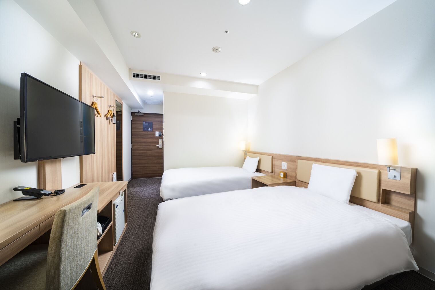 Een hotelkamer met twee bedden, een bureau met een flatscreen televisie, een stoel en een kledingkast.