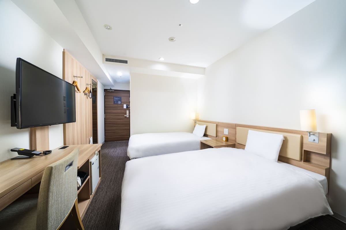 Ett hotellrum med två sängar, ett skrivbord med en platt-TV, en stol och en garderob.