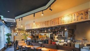 Un restaurant avec un long comptoir, de nombreuses chaises et une cuisine visible au fond de la salle.