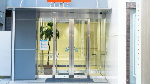 L’entrée d’un hôtel, avec une porte en verre, une enseigne au-dessus indiquant « KOKO », et une petite plante sur le côté gauche.