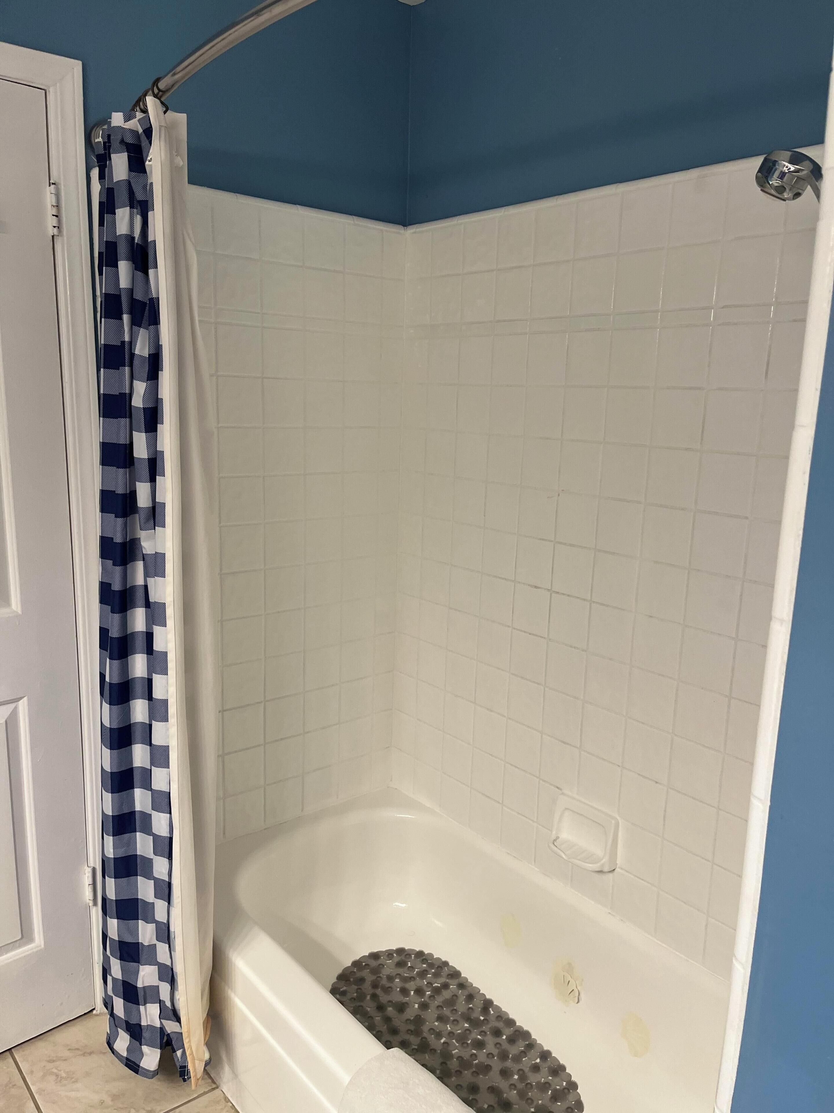 A bathroom with a white bathtub, a shower curtain, and a tiled wall.