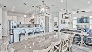 A modern kitchen with white cabinets, stainless steel appliances, and a central island with bar stools. - Estate for Large Groups, Pool & Steps to the Beach (Santa Rosa Beach)