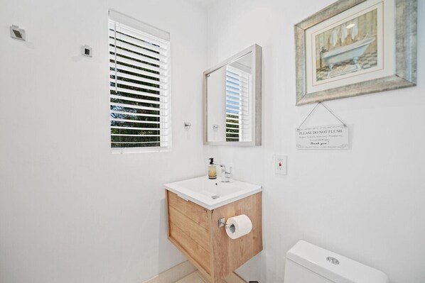 A bathroom with a white sink, wooden cabinet, toilet, and a framed picture on the wall. - Cozy Rustic Getaway in Coral Gables (Coral Gables)