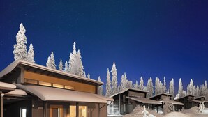 A snow-covered lodge with multiple cabins, a covered walkway, and a car parked in front.
