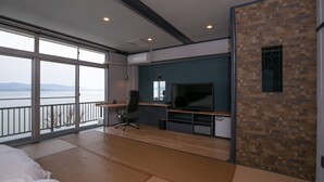 Ein modernes Zimmer mit großem Fenster, einem Bett, einem Schreibtisch mit Computer und einem Fernseher.
