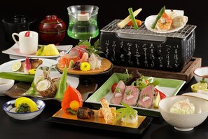 Variedad de platos japoneses sobre una mesa, incluyendo sushi, sashimi y otras exquisiteces, con un set de té y tazas al fondo.