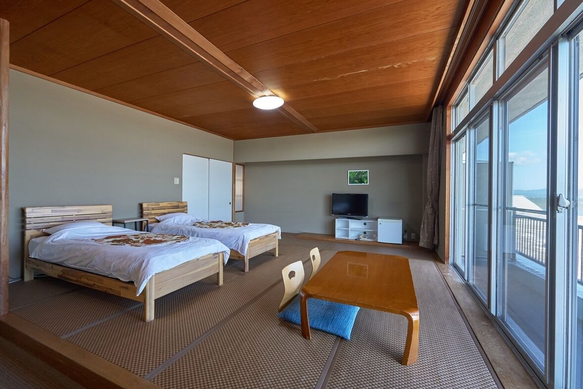 Habitación con dos camas, televisión, mesa y ventanas amplias.