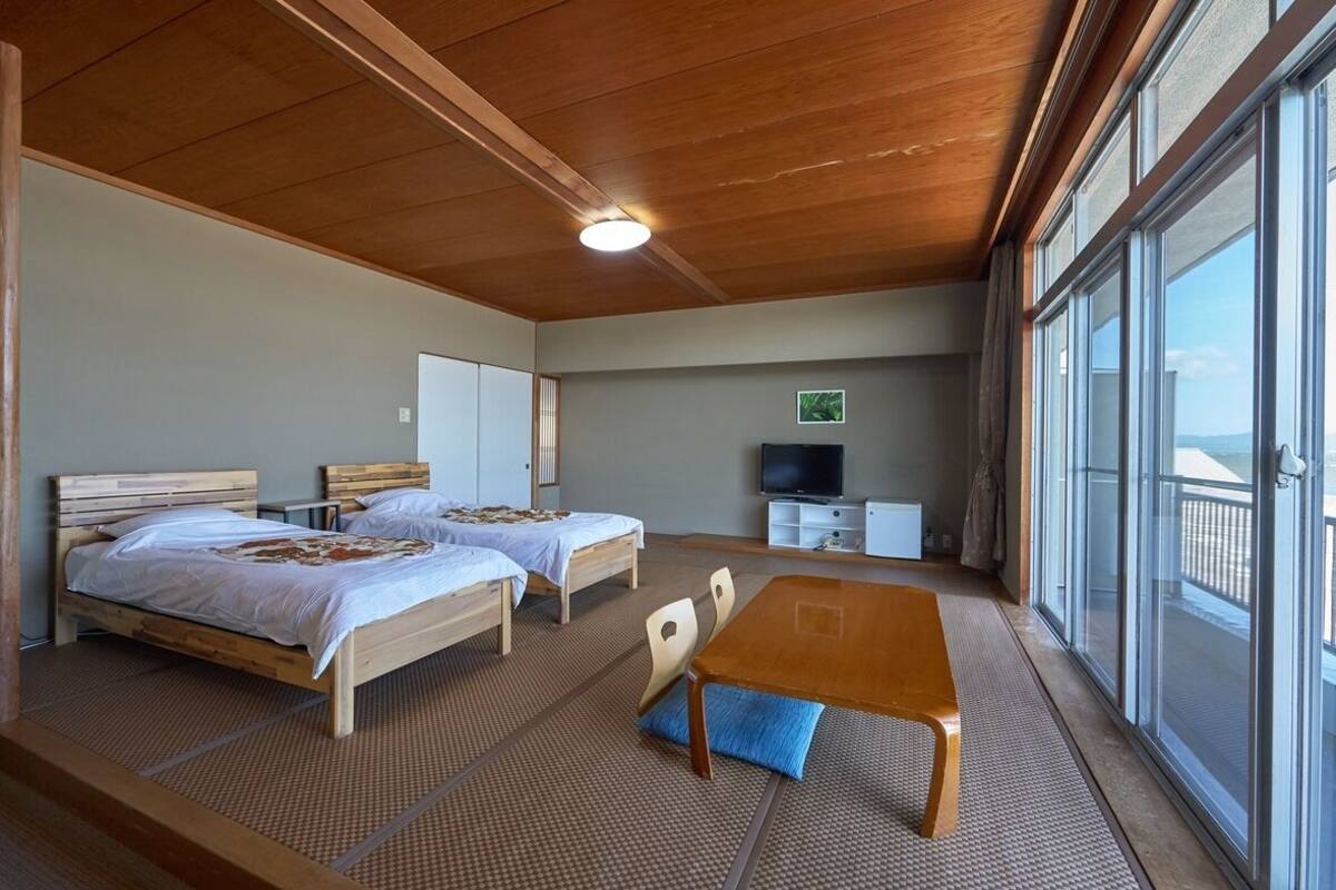Habitación con dos camas, televisión, mesa y ventanas amplias.