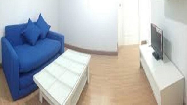 A modern living room with a blue sofa, a white coffee table, and a flat-screen TV on a white stand.