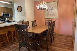 A dining area with a wooden table and chairs, a chandelier, a clock, and a framed map on the wall. - Great Value Close to Resort-Heated Pool-HotTubs-Grills-Looping Ski Shuttle-Parking Near Unit-Updates (Steamboat Springs)