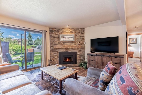 A living room with a stone fireplace, a flat-screen TV, and a large sliding glass door to a patio.