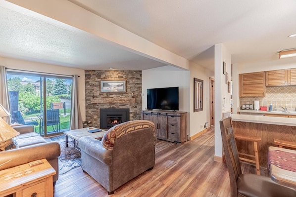 A living room with a fireplace, a television, and a dining area with wooden cabinets. - Great Value Close to Resort-Heated Pool-HotTubs-Grills-Looping Ski Shuttle-Parking Near Unit-Updates (Steamboat Springs)