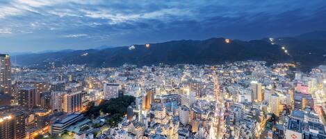 A cityscape at dusk with illuminated buildings and a mountain range in the background.