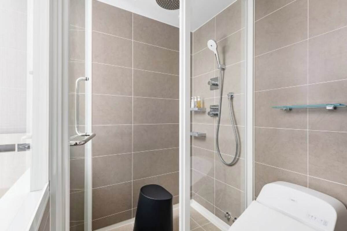 A modern bathroom with a glass shower enclosure, a white toilet, and a small shelf with toiletries.