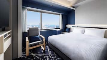 Une chambre d’hôtel moderne, dotée d’un grand lit, d’un bureau, d’une chaise et offrant une vue sur la ville par la fenêtre.