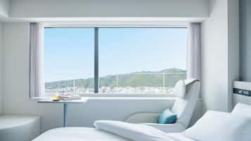 Una habitación de hotel moderna con un ventanal grande, una cama, un área de descanso y una mesita con una taza y vasos.