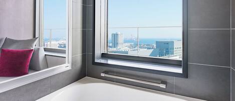 A modern bathroom with a large bathtub, a window with a city view, and a towel rack.