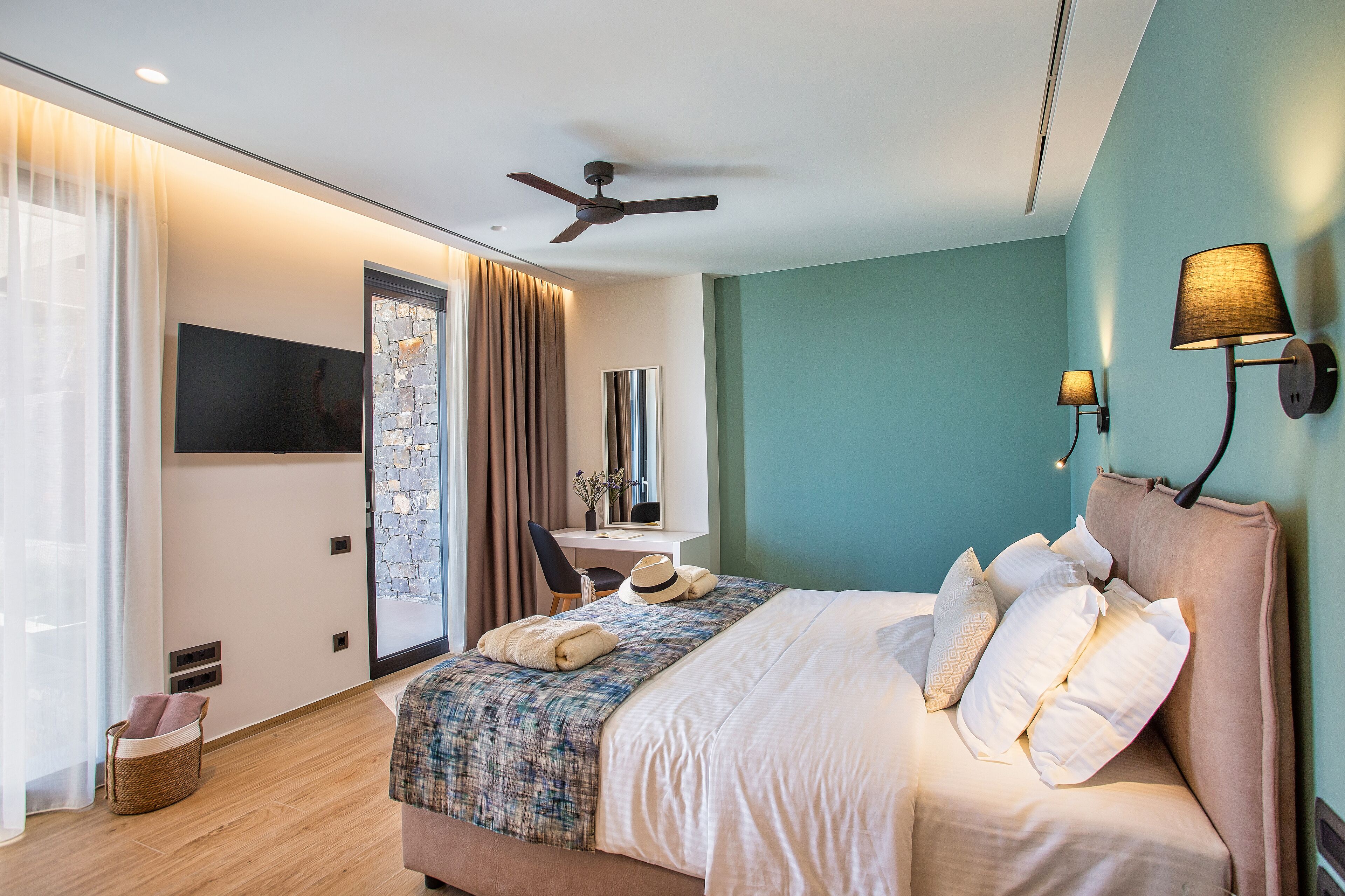 Ein modernes Hotelzimmer mit Bett, Schreibtisch, Stuhl, Fernseher und Deckenventilator.