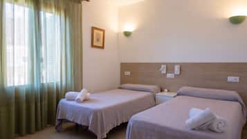 A hotel room with two single beds, a window with green curtains, a wall-mounted light, and a framed picture.
