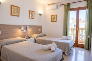 A hotel room with two beds, a wooden headboard, wall-mounted lights, framed botanical prints, and a sliding glass door to the outside. - Family House in Port of Alcudia | Pool, Terrace & 11 min Walk to Beach (Puerto de Alcudia)