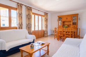Uma sala de estar com sofá, mesa de madeira, mesa de jantar com cadeiras e aparador de madeira com prateleiras.