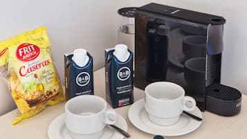 A breakfast setup with two white cups, a bag of Frit Ravich Caseras chips, two B&B Hotels milk cartons, and a coffee maker.