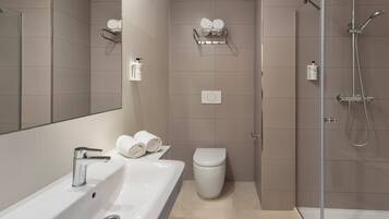 A modern bathroom with a white sink, toilet, and shower. There are two towel racks on the wall, and a bottle of hand soap is visible.