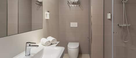 A modern bathroom with a white sink, toilet, and shower. There are two towel racks on the wall, and a bottle of hand soap is visible.