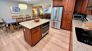 Une cuisine moderne avec des meubles en bois, un réfrigérateur en acier inoxydable, un four encastré et un coin repas comprenant une table et des chaises.