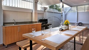 A modern kitchen with wooden cabinets, a built-in oven, and a dining area with a long table and four wine glasses. - Gala Express (Pattaya)