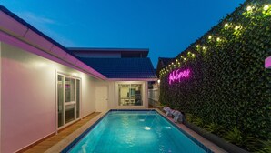 A swimming pool with a tiled deck, a glass door entrance, and a neon sign on the wall. - Gala Express (Pattaya)